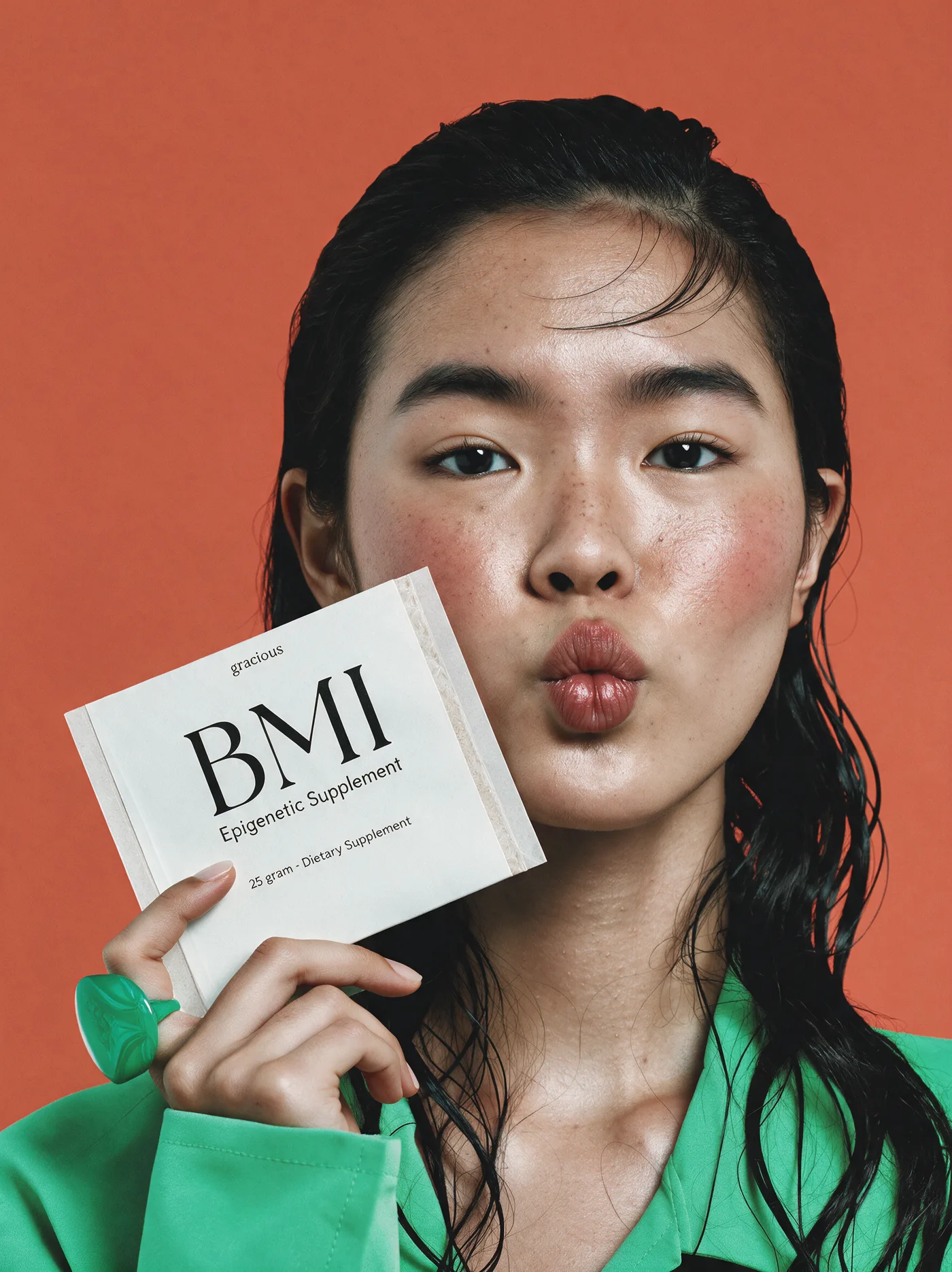 A person holding a BMI sachet to their face against a coral backdrop